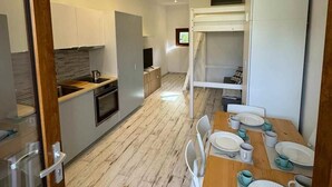 Eine moderne Küche mit weißen Schränken, einer Holzarbeitsplatte und einem eingebauten Backofen. Es gibt eine Essecke mit einem Holztisch für zwei Personen, weißen Stühlen und einer Fußmatte mit der Aufschrift 'WELCOME'.