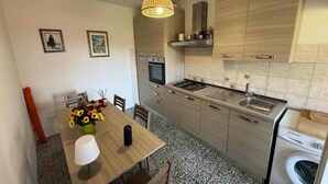 A compact kitchen with a dining area, a washing machine, and a hanging light fixture.