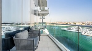 Un balcón con vista a un puerto deportivo, mobiliario moderno y baranda de vidrio.