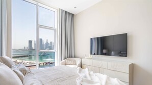 Un dormitorio moderno con un ventanal grande, una cama, un televisor y vistas a la ciudad y al frente marítimo.