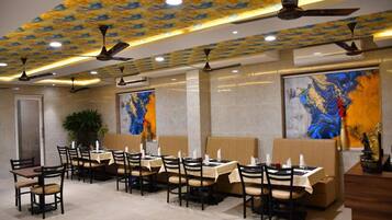 A restaurant with multiple dining tables and booths, ceiling fans, and large abstract paintings on the walls.
