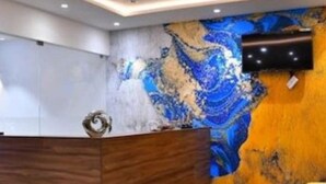 A reception area with a marble wall, a wooden reception desk, and a yellow chair. - HOTEL ADHIKRISHNA ARCADE (Erode)