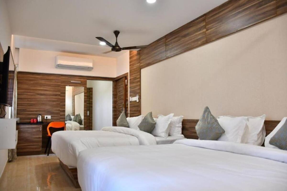 Habitación de hotel con dos camas, un ventilador de techo, un equipo de aire acondicionado, un escritorio pequeño con una silla y un espejo en la pared.