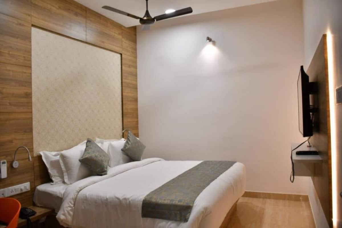 Una habitación de hotel moderna con una cama grande, un ventilador de techo, un televisor montado y una pared decorativa de madera.