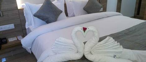Een hotelkamer met een net opgemaakt bed, kussens en een zwaan van handdoeken op het bed.