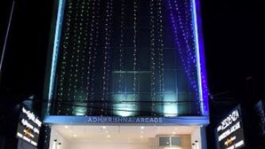 A building with a modern facade, a visible entrance, and a car parked in front. - HOTEL ADHIKRISHNA ARCADE (Erode)