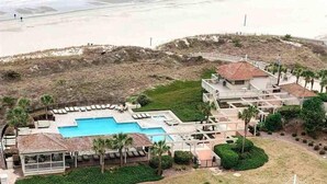 A resort with a swimming pool, lounge chairs, and a beach view.