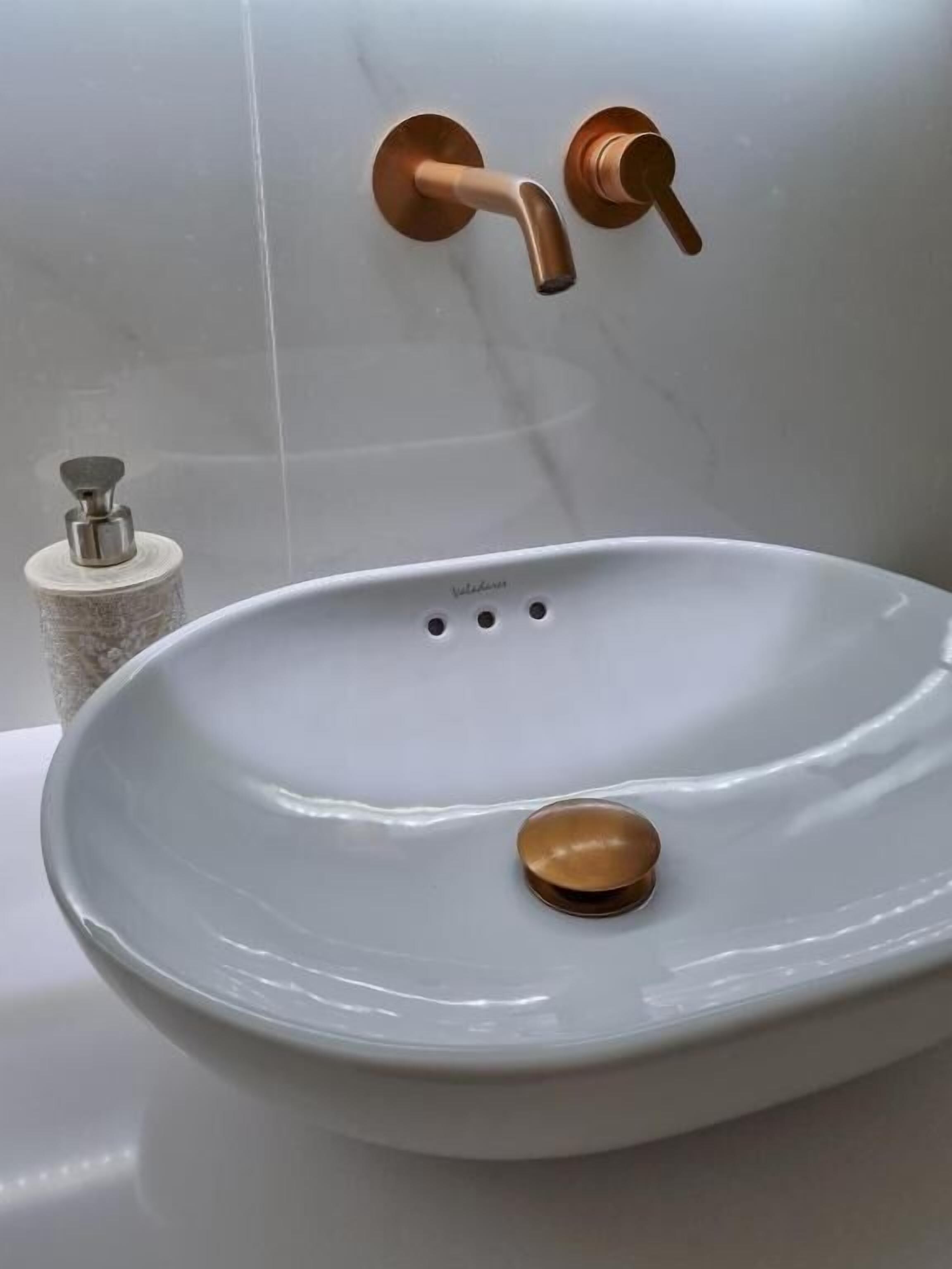 A bathroom with a white sink, a copper faucet, and a soap dispenser.