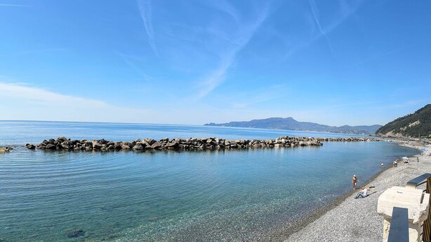 Une vue dégagée sur la côte, avec un brise-lames rocheux, une mer calme et une plage de galets.