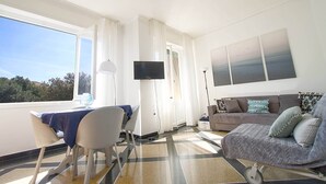 Une pièce comprenant une table à manger, des chaises, un canapé, un téléviseur et donnant sur l’extérieur.
