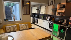 A modern kitchen with white cabinets, a dining table, and a seating area with yellow cushions. - Sheffield Spacious 4 Bedroom House-all En-suites (Sheffield)