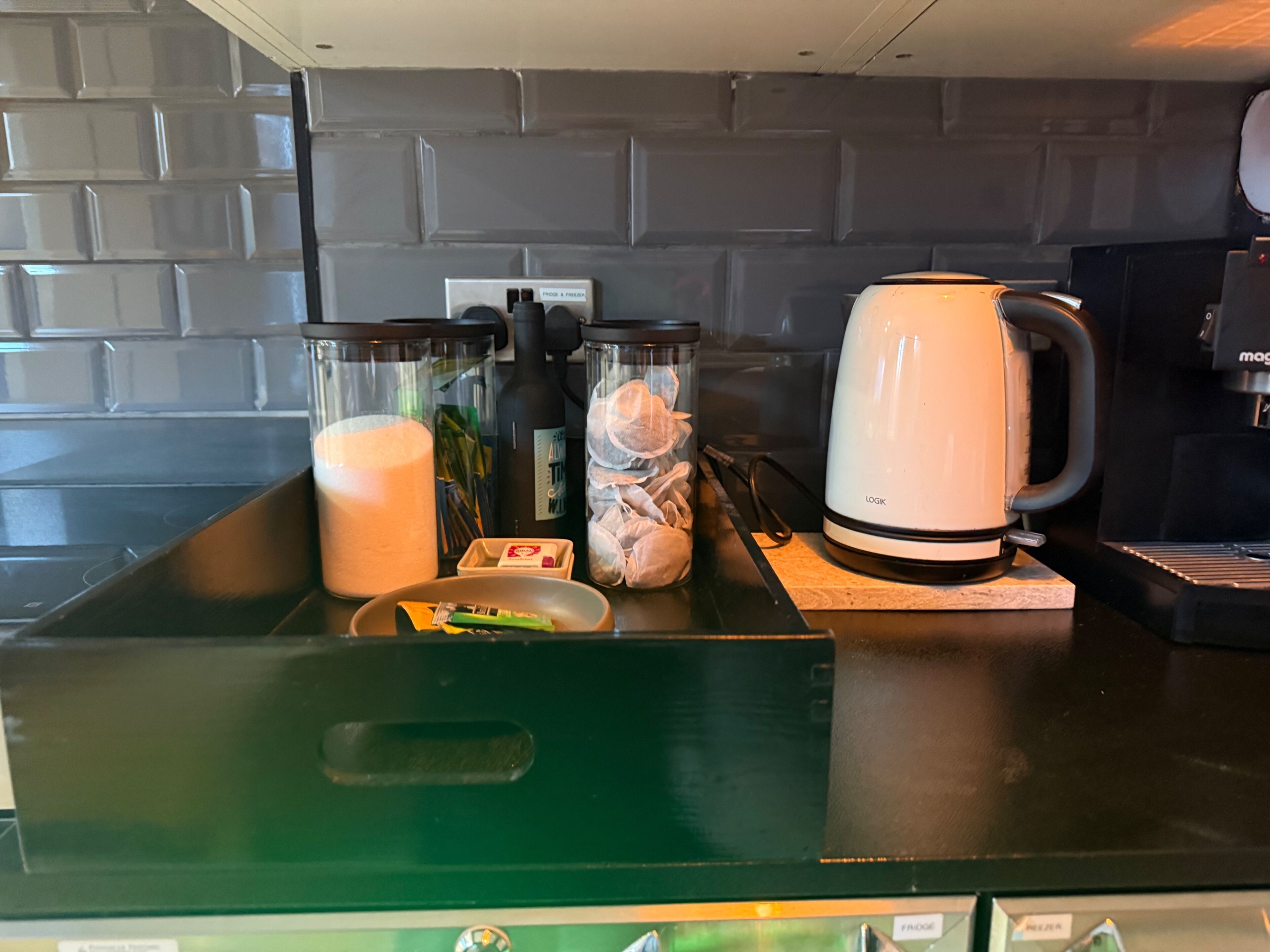 Una encimera de cocina con una cafetera, un espumador de leche y frascos de especias.