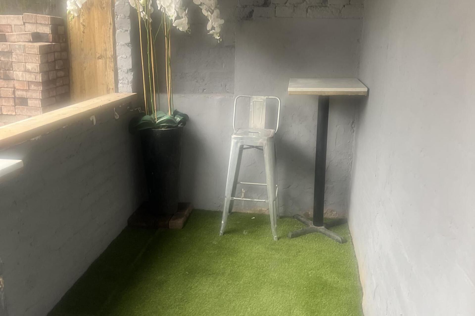 A small room with a green artificial grass floor, a white chair, a small table, and a brick wall.