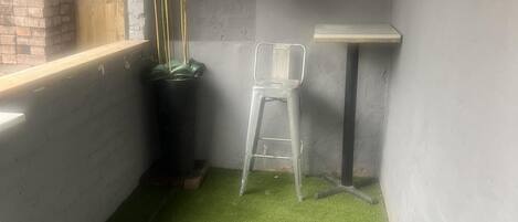 A small room with a green artificial grass floor, a white chair, a small table, and a brick wall.