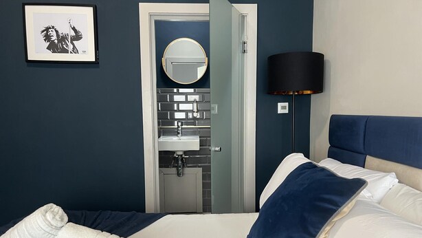 A hotel room with a bed, a bedside lamp, a bathroom visible through an open door, and a framed picture on the wall. - Sheffield Spacious 4 Bedroom House-all En-suites (Sheffield)