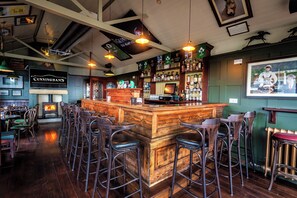 Una zona de bar con taburetes de madera, un mostrador con una caja registradora y una variedad de botellas de licores.