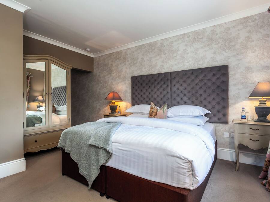 A bedroom with a large bed, a wardrobe, a bedside table with a lamp, and a mirror.