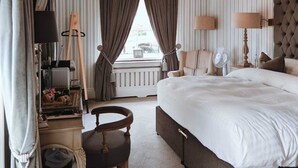 Habitación de hotel con una cama grande, una zona de estar con una silla, un escritorio con lámpara y un ventanal con cortinas.