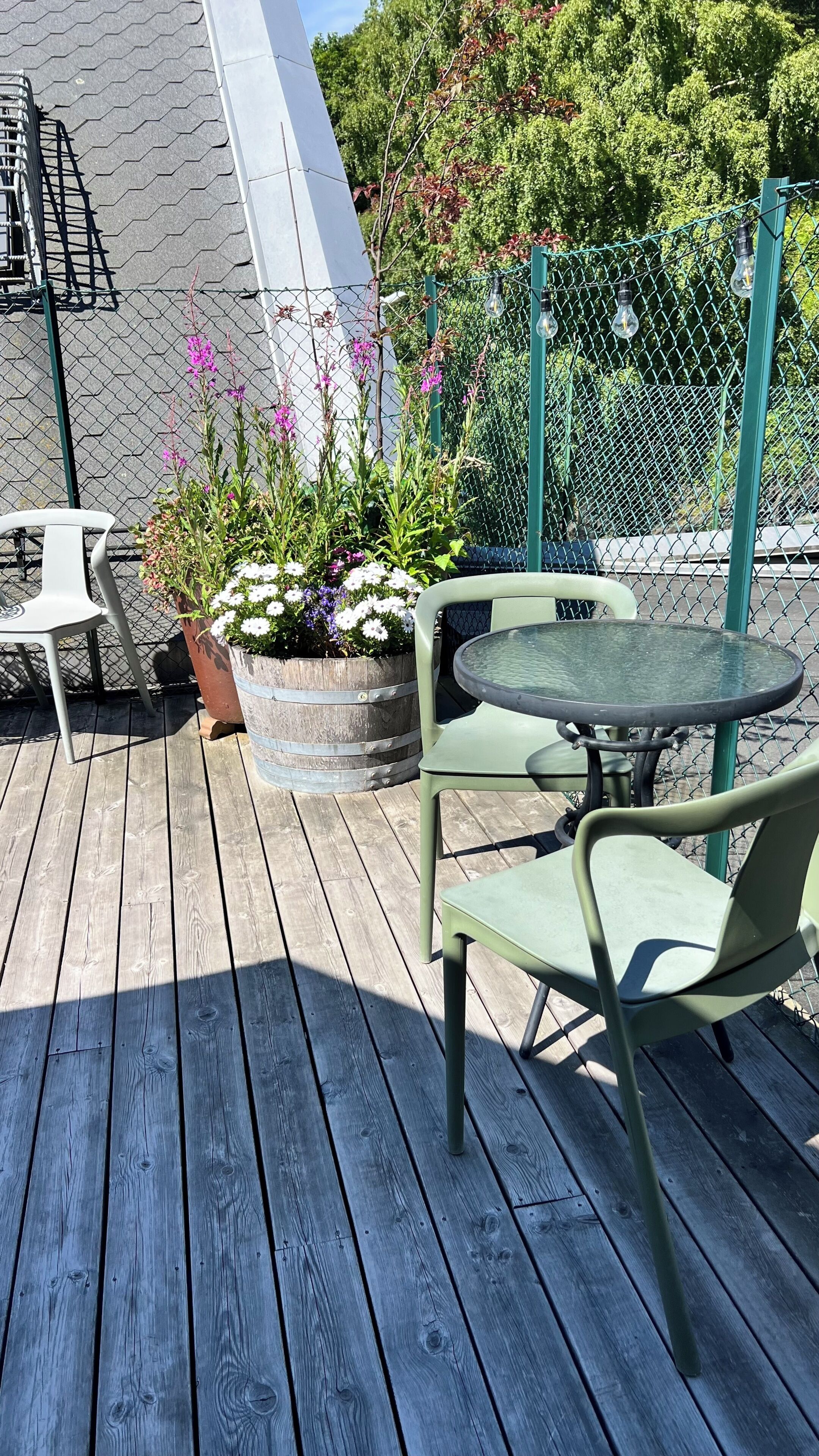 Una terraza de madera con mobiliario exterior, que incluye una mesa y sillas, y una jardinera con flores.
