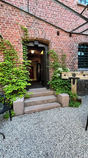 A brick building with a wooden gate, steps leading to an entrance, and greenery around. - Fengselshotellet (Arendal)