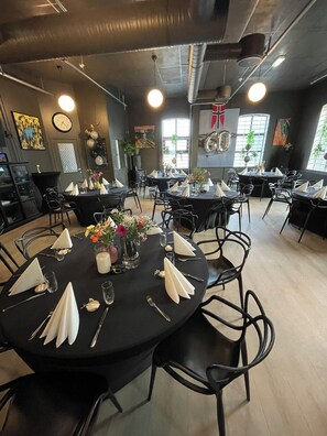 A restaurant with round tables set for dining, black chairs, and a modern industrial ceiling. - Fengselshotellet (Arendal)