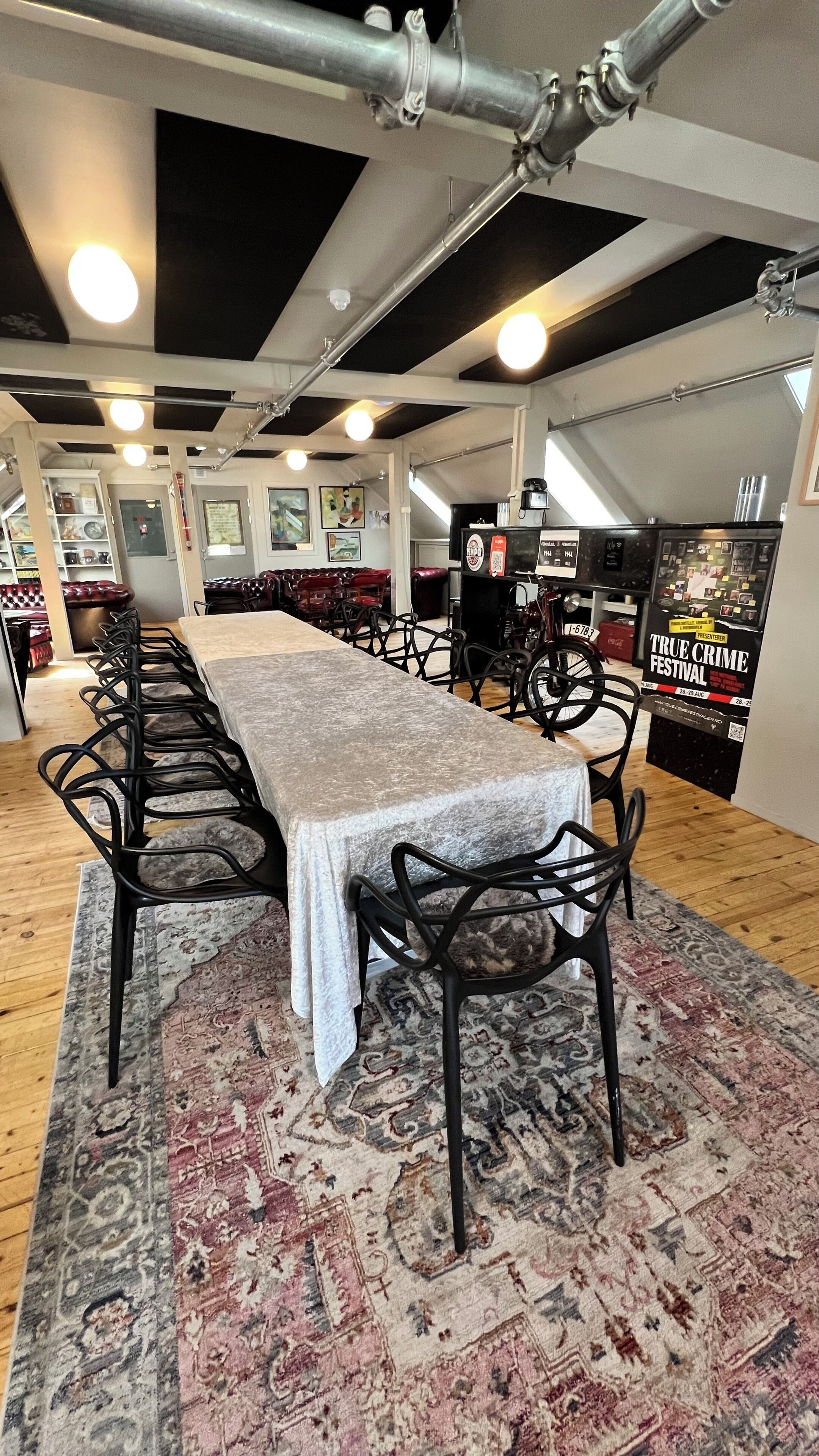 A long table with chairs, a patterned rug, and a black metal ceiling structure.