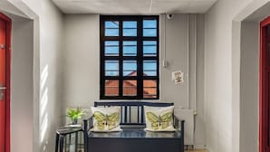 A narrow hallway with a black bench, a window, and a radiator. - Fengselshotellet (Arendal)