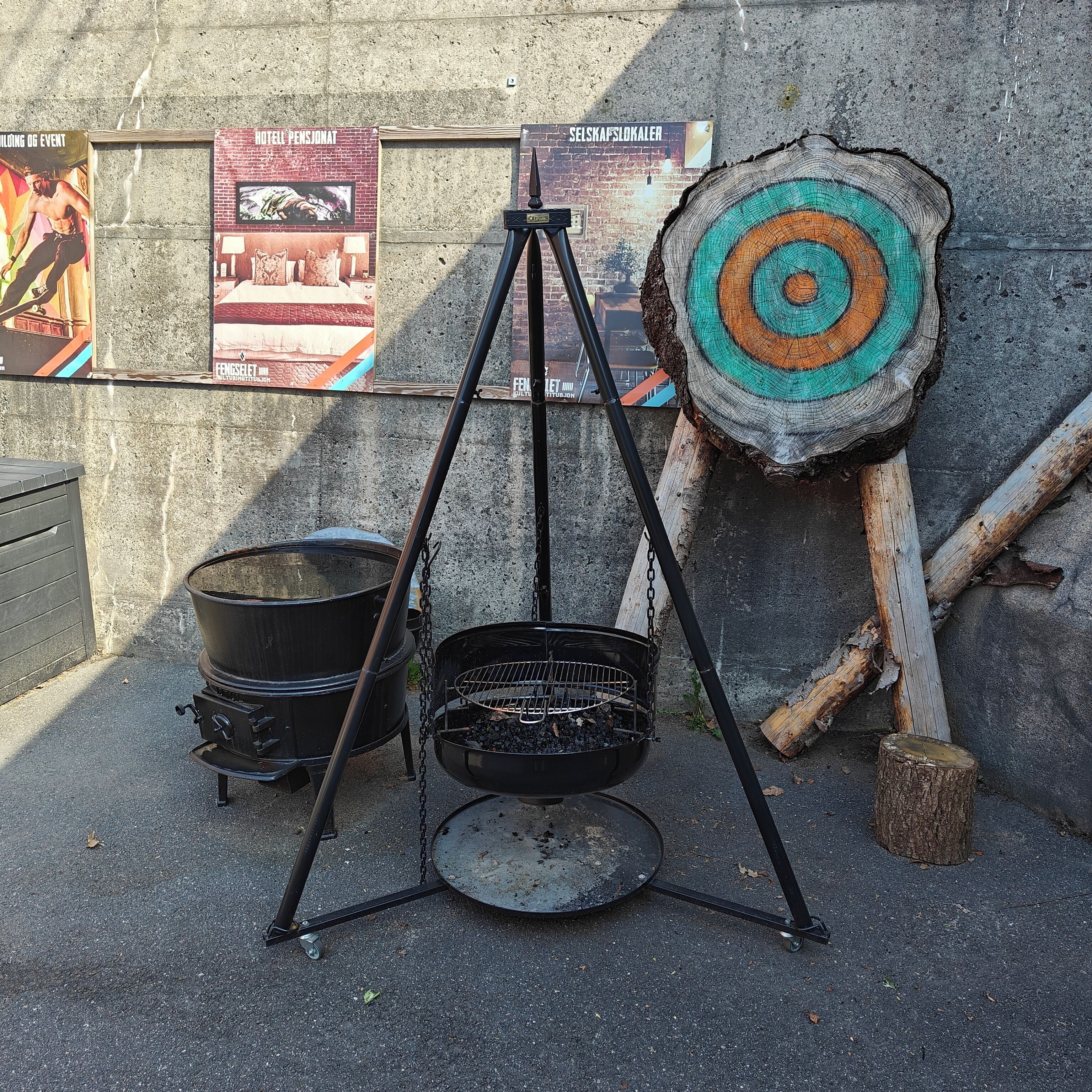A portable grill setup with a metal pot and a hanging pot, a target board, and a wooden post.