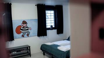 Una habitación con una cama, un ventanal con cortinas, un estante en la pared con zapatos y un personaje de dibujos animados en la pared.