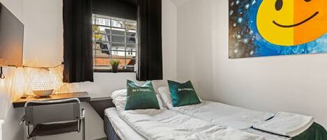 A hotel room with a bed, a desk with a lamp, a chair, and a window with curtains.