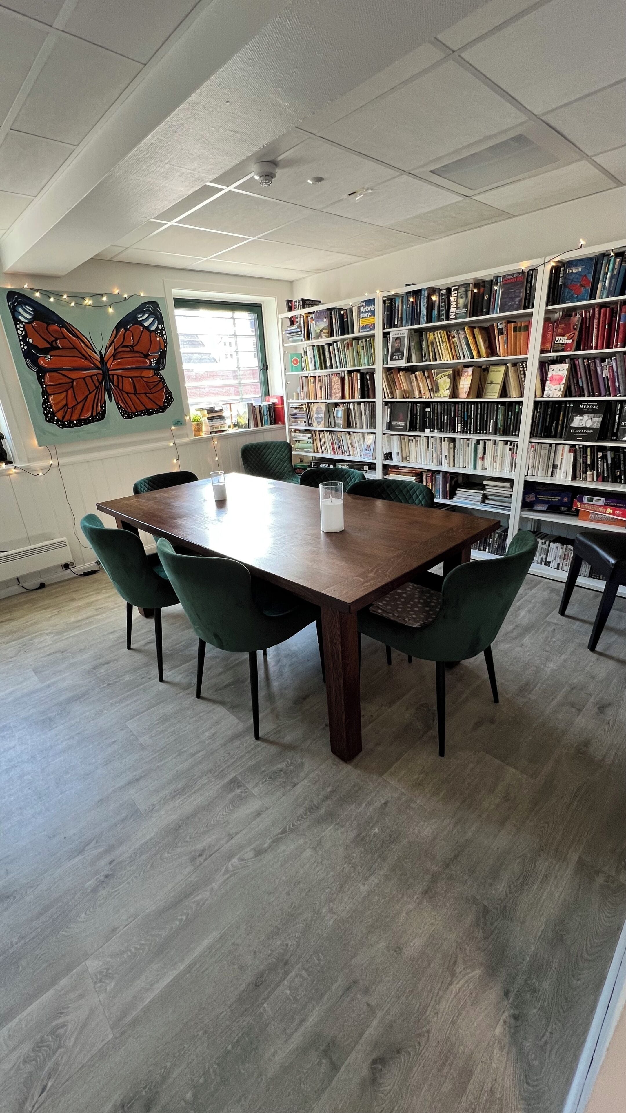 A library with a wooden table, green chairs, and bookshelves filled with books.