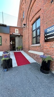 A brick building with a red carpet entrance, a sign for 'INNGANG,' and directional signs for 'SELSKAP LOKALER,' 'RESEPSJOG,' and 'CATERING.'