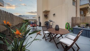 An outdoor patio with a wooden table and chairs, surrounded by potted plants and a bamboo fence.
