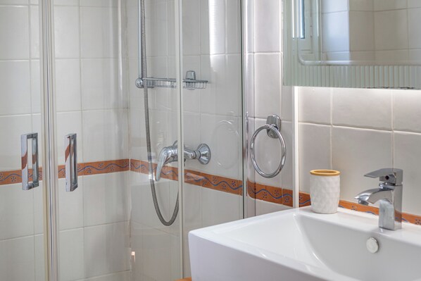 Une salle de bain avec une douche à parois de verre, un lavabo avec un miroir et un porte-serviettes.