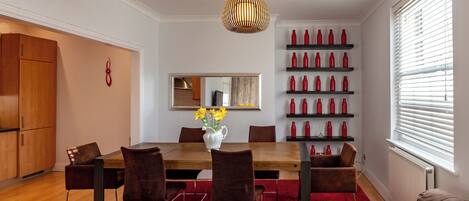 Uma sala de jantar moderna com mesa de madeira, cadeiras marrons e tapete vermelho. Há um vaso com flores amarelas sobre a mesa.