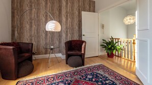 Ein Zimmer mit einer Holzwand, einem gemusterten Teppich, zwei Ledersesseln, einer Stehlampe und einem Blumentopf.