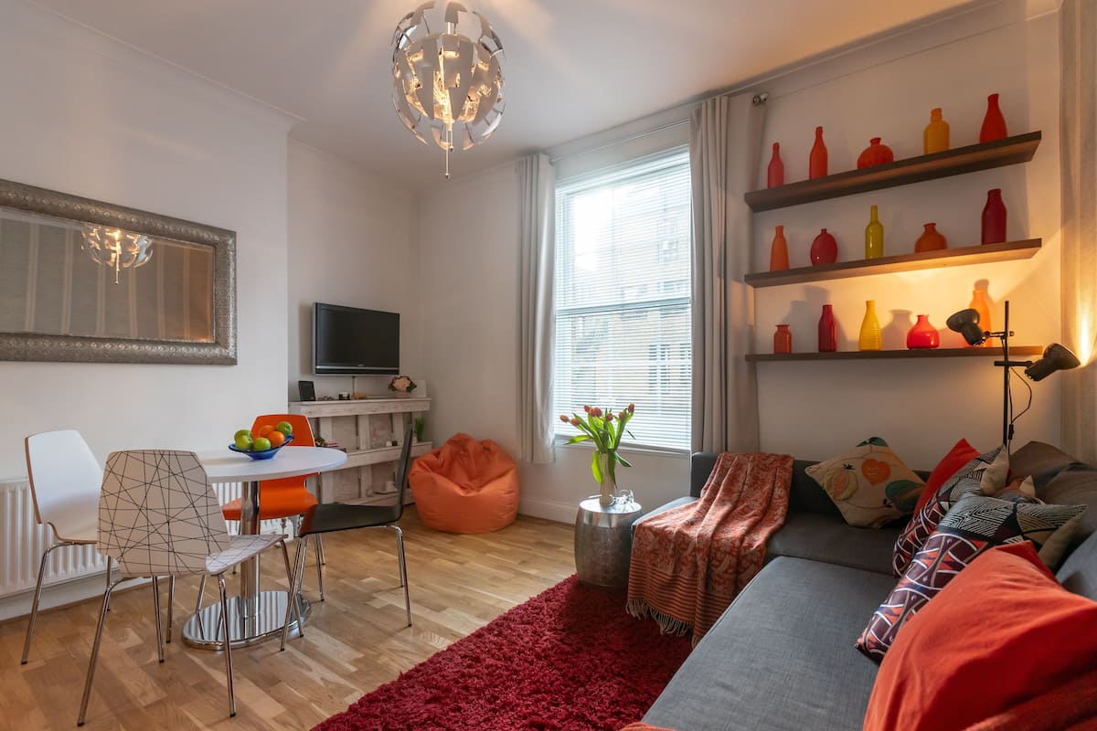 A modern living room with a sofa, a dining table with chairs, a TV, and a red rug.