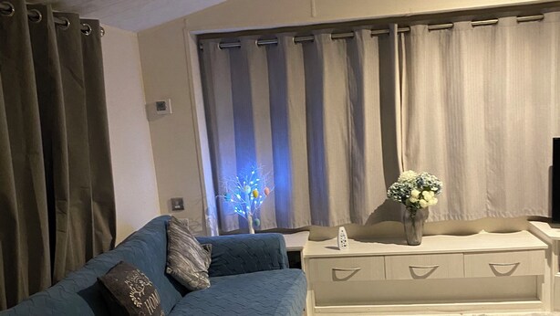 A living room with a blue sofa, a white side table with a vase, and a grey shag rug. - Immaculate 3-bed Caravan 10mins From Gt Yarmouth (Great Yarmouth)