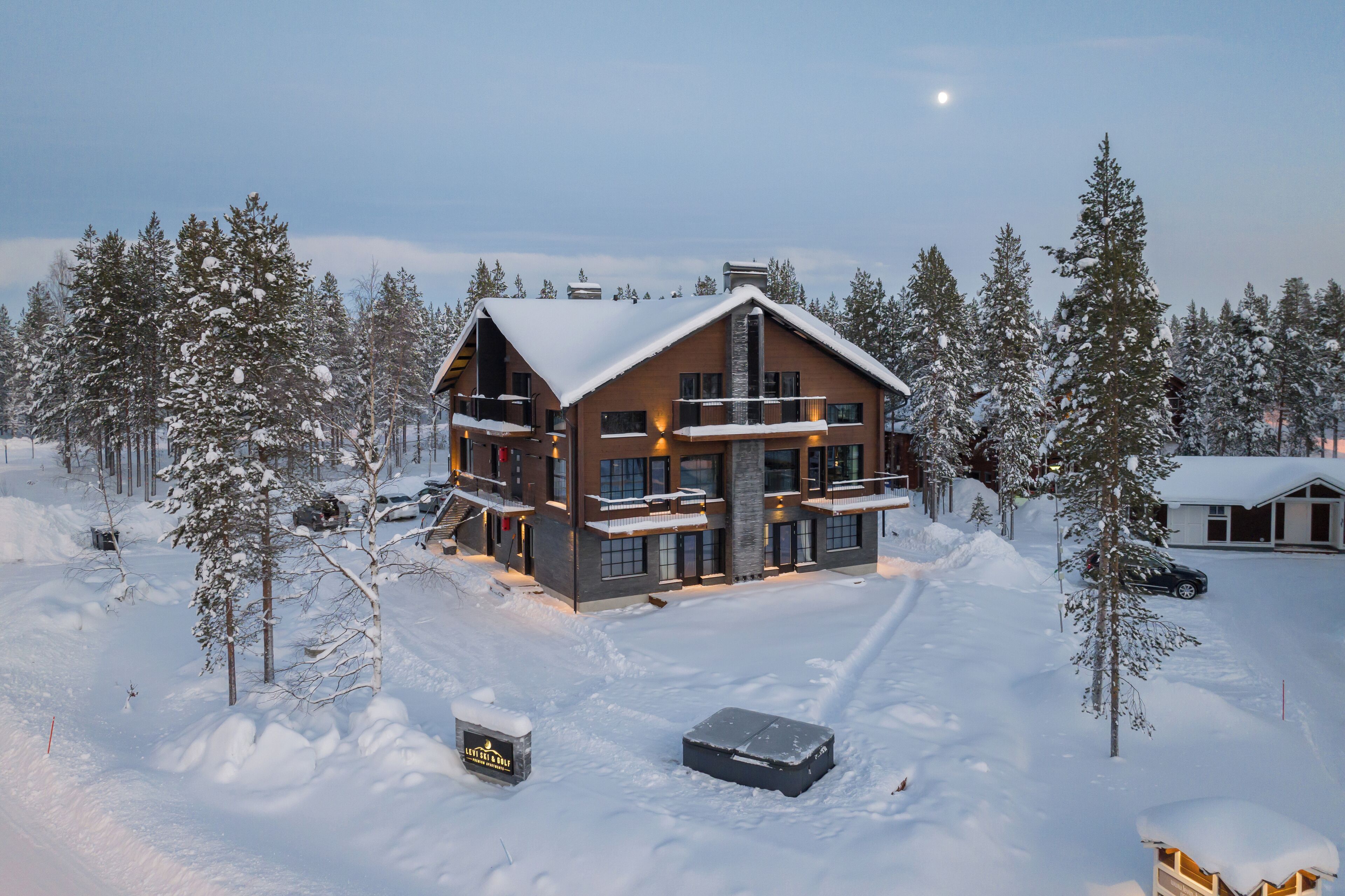 A large, multi-story lodge with a snow-covered roof and multiple balconies, surrounded by snow-laden trees.