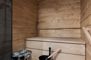 A sauna room with wooden walls and benches, a metal bucket with rocks, and a wooden ladle.