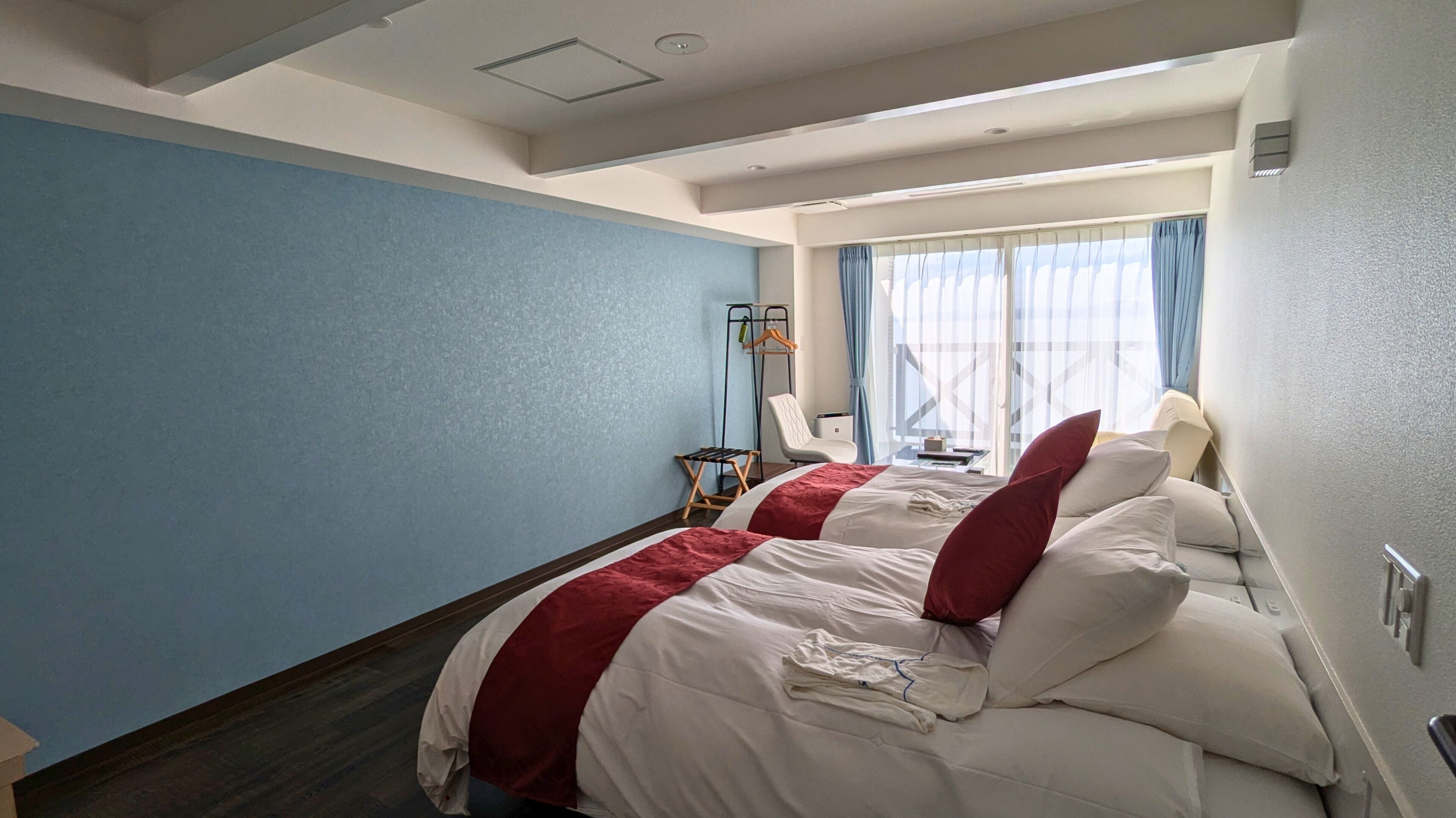 Ein Hotelzimmer mit Bett, Stuhl, Fenster mit Vorhängen und Deckenleuchte.