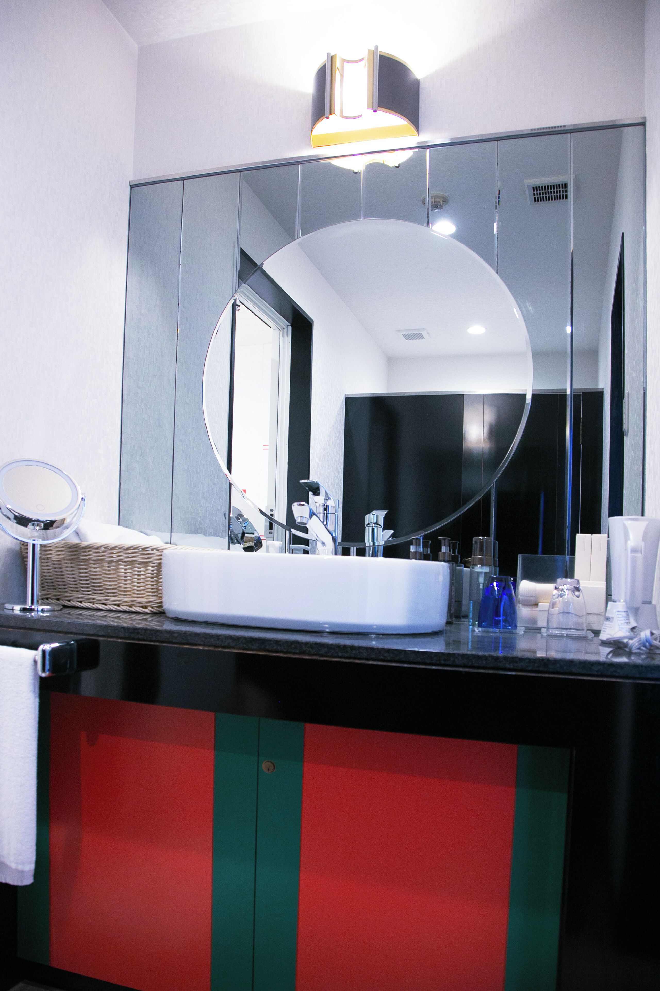 Un baño con un espejo grande, un lavabo blanco y un mueble de armario rojo y verde.