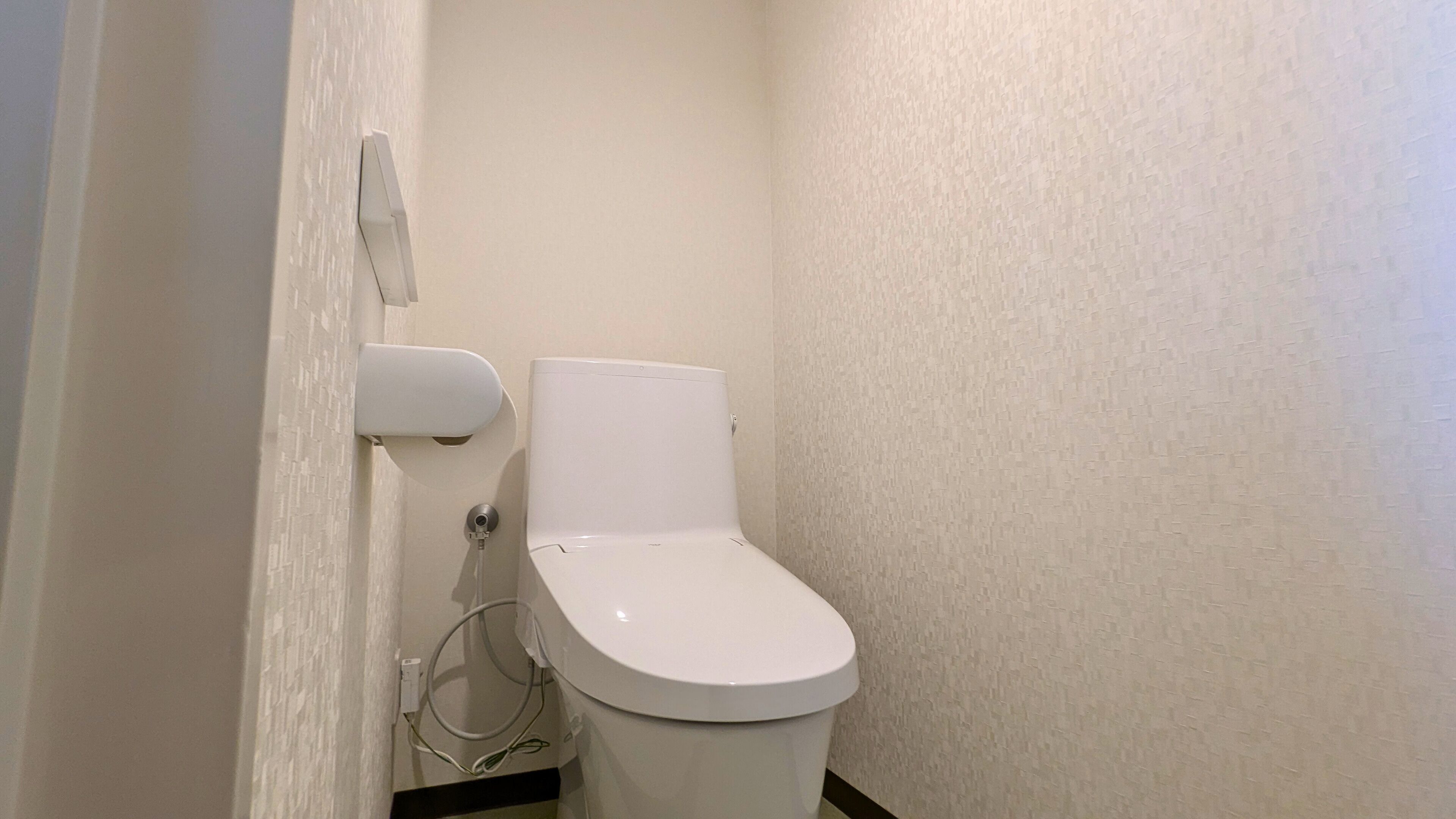 A small, white toilet with a flush handle and a paper towel dispenser mounted on the wall.