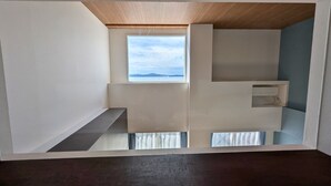 Une pièce avec un plafond en pente, une fenêtre donnant sur la mer et une étagère intégrée.