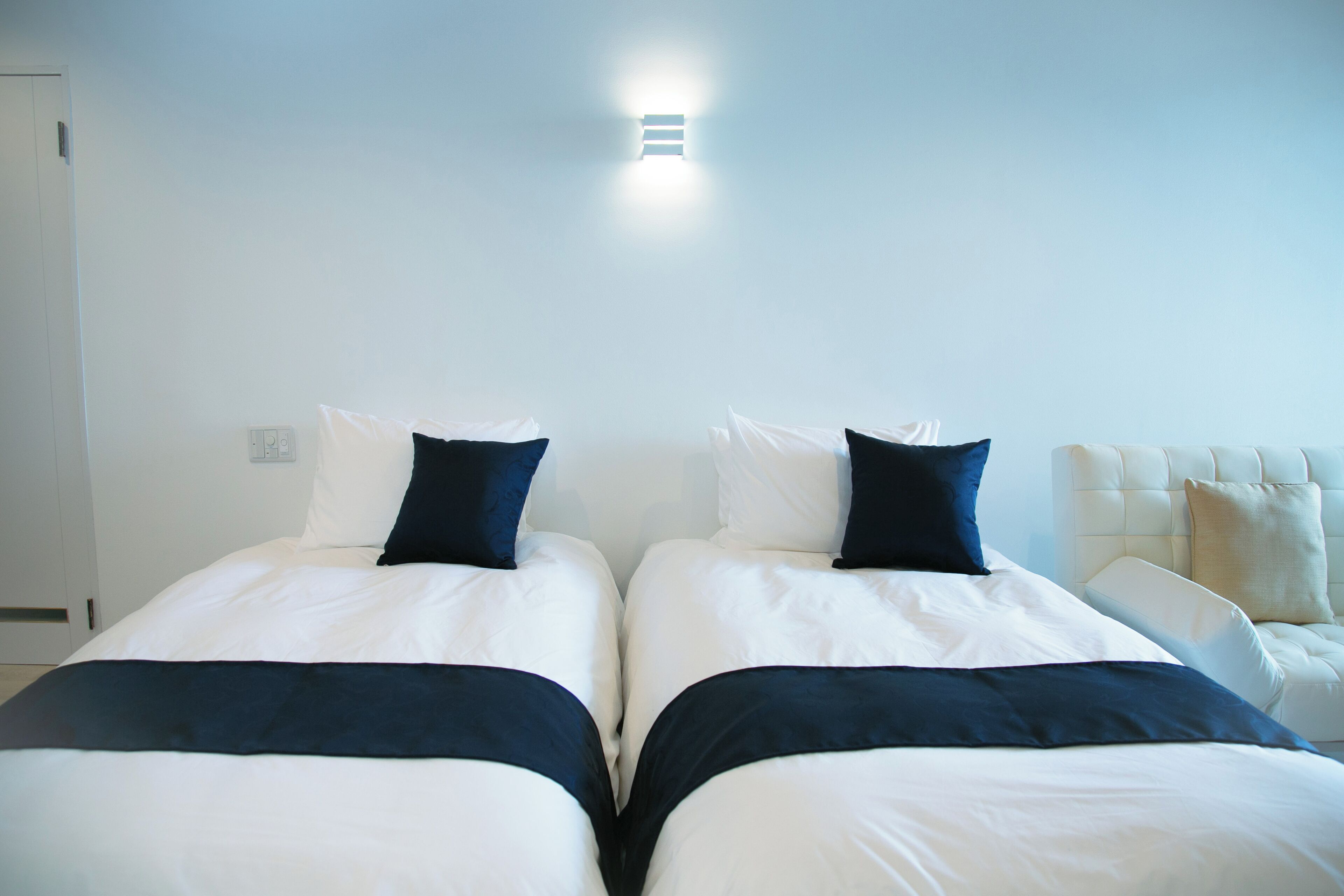 A double bed with white and navy bedding, a bedside table, and a wall-mounted light fixture.
