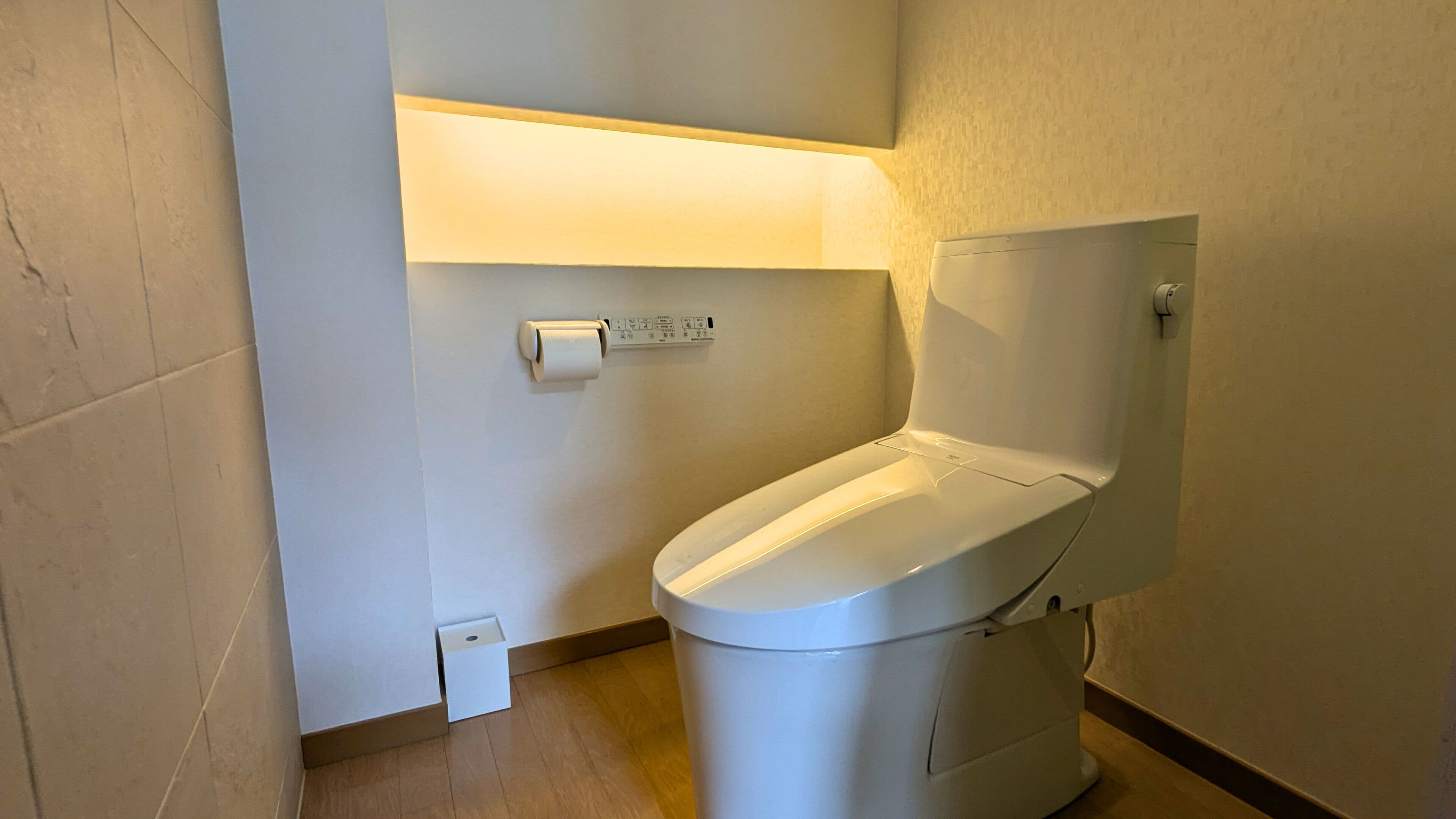 Une salle de bain moderne avec des toilettes blanches, un réservoir de chasse d'eau fixé au mur et un porte-rouleau de papier toilette.