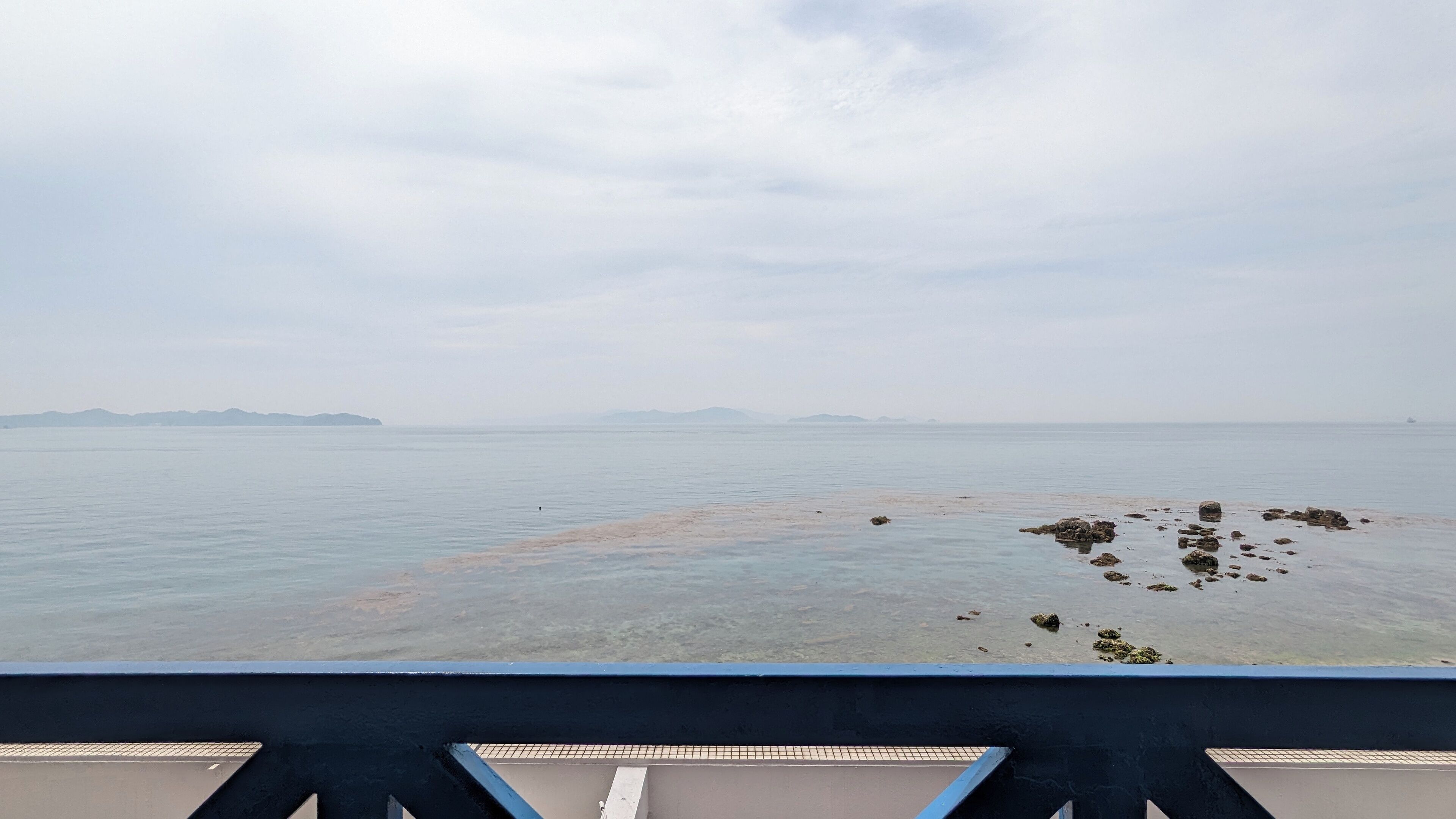 A view of a calm sea with distant landforms and a rocky shoreline.