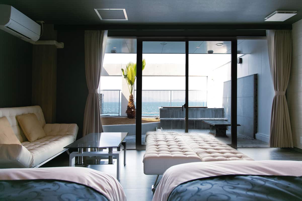 Une chambre d’hôtel moderne avec un canapé, un lit, une petite table et un balcon donnant sur la mer.