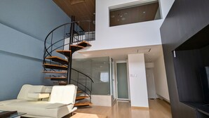Un salon moderne avec un escalier en colimaçon, un canapé blanc et une porte en verre donnant sur une autre pièce.