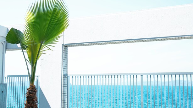Un balcon blanc avec une balustrade en métal donnant sur une mer d’un bleu limpide.